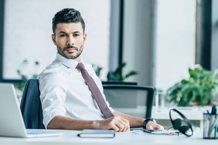 confident businessman looking at camera while sitting at workplaceの写真素材
