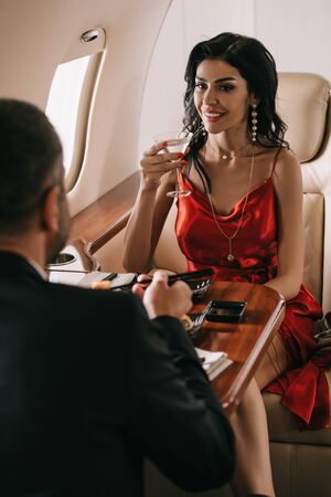 selective focus of elegant woman in red dress holding martini glass and looking at man in private...