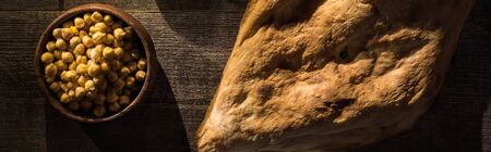 top view of delicious chickpeas in bowl near fresh baked pita on wooden rustic table, panoramic shot