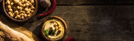 top view of delicious hummus, chickpeas, pita, spices on wooden rustic table, panoramic shotの写真素材