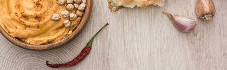 top view of delicious hummus with chickpeas in bowl near fresh baked pita and spices on beige wooden table, panoramic shotの写真素材