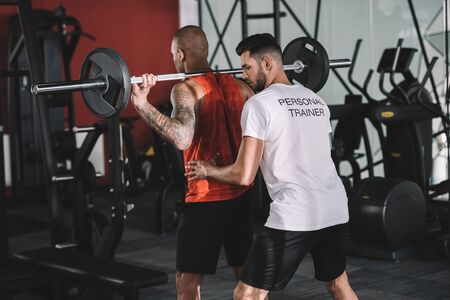 personal trainer supporting african american sportsman lifting barbell