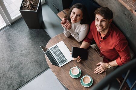 overhead view of smiling young couple working on laptop in coffee shop