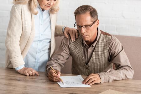 cropped view of senior woman standing near husband with mental illness drawing on paperの写真素材