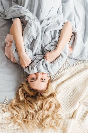 top view of young woman covering face with blanket and looking at cameraの写真素材