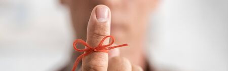 panoramic shot of red bow on finger of senior man with mental illnessの写真素材