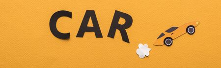 top view of paper cut sports car with exhaust gas and black car lettering on orange background,...
