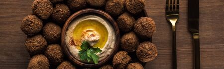 top view of falafel balls with hummus on plate near cutlery on wooden table, panoramic shotの写真素材