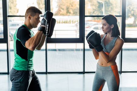 sportswoman in boxing gloves working out with sportsman in sports centerの写真素材