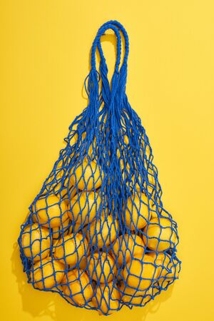 top view of ripe lemons in string bag on yellow backgroundの写真素材