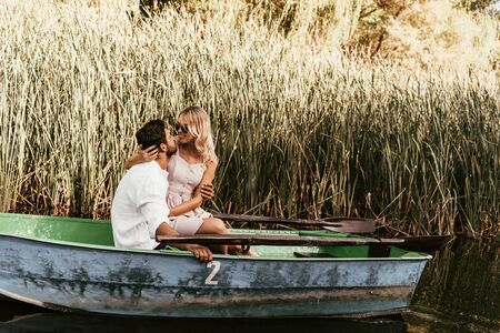 young couple hugging and kissing in boat on river near thicket of sedgeの写真素材