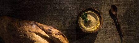 top view of delicious hummus in bowl near fresh baked pita and spoon on wooden rustic table, panoramic shotの写真素材