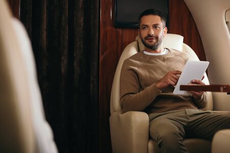 selective focus of handsome bearded man using digital tablet in private jet