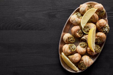top view of delicious cooked escargots with lemon on black wooden tableの写真素材