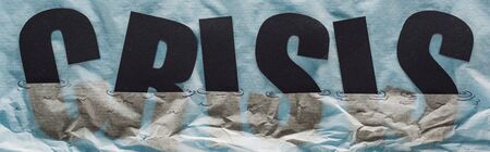 panoramic shot of black word crisis sinking in paper symbolizing water on grey paper backgroundの写真素材