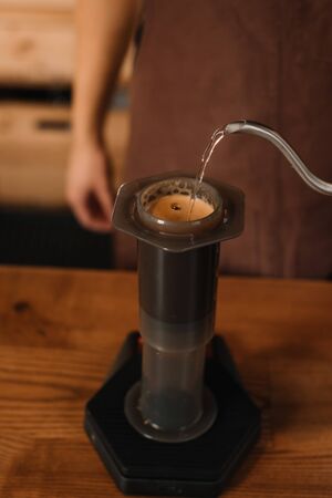 cropped view of barista pouring water from kettle in aeropress while preparing coffeeの写真素材