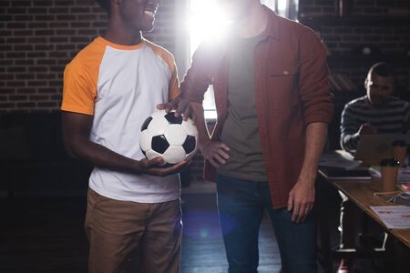 cropped view of african american businessman holding soccer ball near colleague standing with hand on hipの写真素材