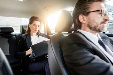 selective focus of attractive ambassador holding papers near briefcase while sitting in car with manの写真素材