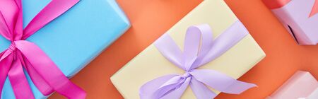 top view of multicolored gift boxes with ribbons and bows on orange background, panoramic shotの写真素材