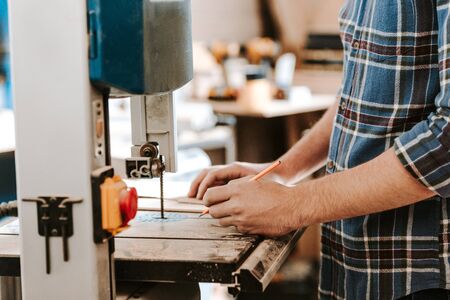 cropped view of carpenter holding pencil near electric woodworking in workshopの写真素材