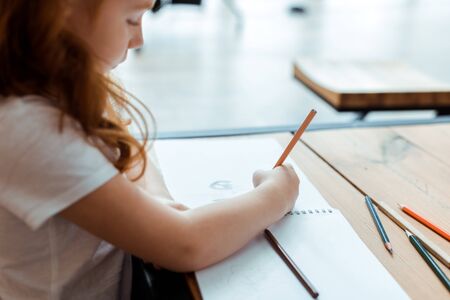 selective focus of redhead kid drawing on paper with color pencilの写真素材