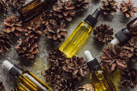 top view of bottles with natural oil near dry spruce cones on grey stone surface