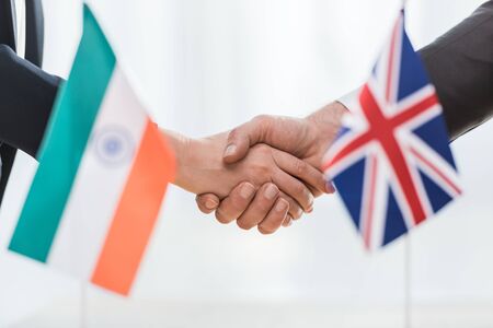 cropped view of diplomats shaking hands near flags of india and united kingdomの写真素材