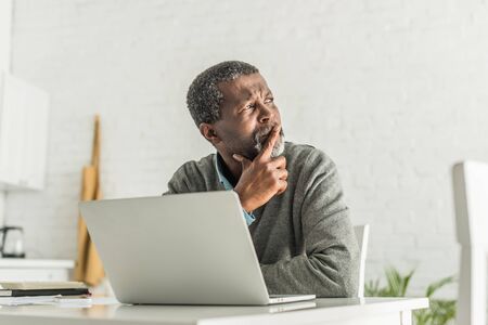 thoughtful african american man looking away while sitting near laptopの写真素材