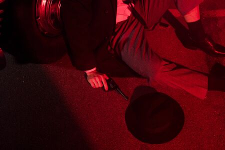 cropped view of gangster holding gun while sitting near hat and retro car