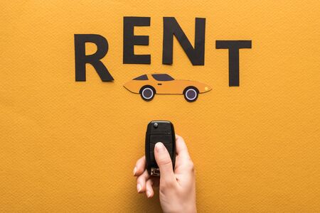 cropped view of woman holding car key near paper cut auto and black rent lettering on orange backgroundの写真素材