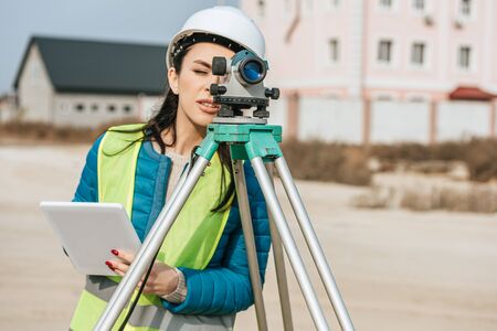Female surveyor with digital tablet looking through measuring levelの写真素材