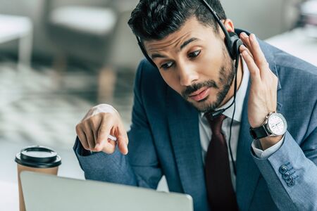 concentrated call center operator in headset pointing with finger at laptopの写真素材