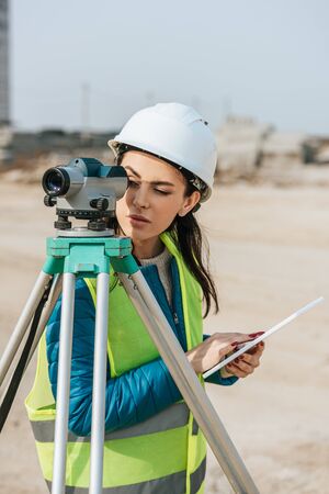 Surveyor with digital tablet looking through measuring levelの写真素材