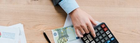 panoramic shot of man using calculator near euro banknote