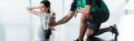 panoramic shot of sportswoman doing crunches and sportsman helping her in sports center