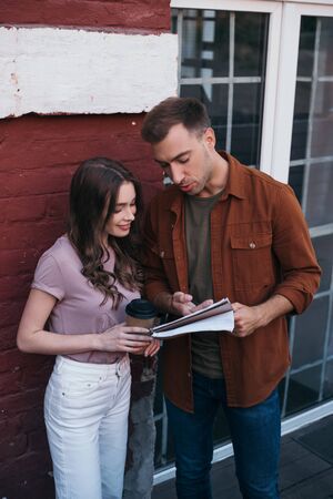 thoughtful businessman showing documents to smiling colleague holding coffee to goの写真素材