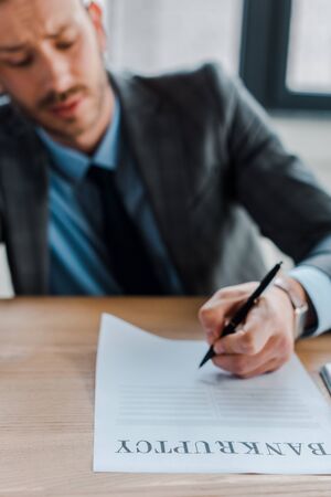 selective focus of businessman holding pen near paper with bankruptcy lettersの写真素材