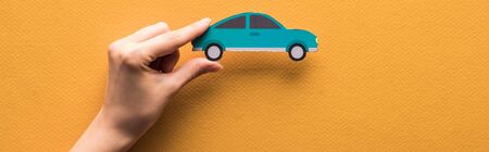 cropped view of woman holding paper cut car on orange background, panoramic shotの写真素材