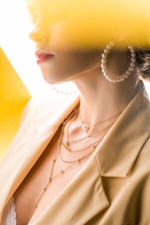 cropped view of young woman in necklace and earrings on orange and whiteの写真素材