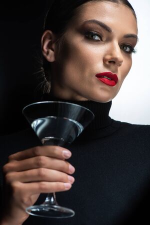 beautiful elegant woman with red lips holding martini and looking at camera isolated on white and blackの写真素材