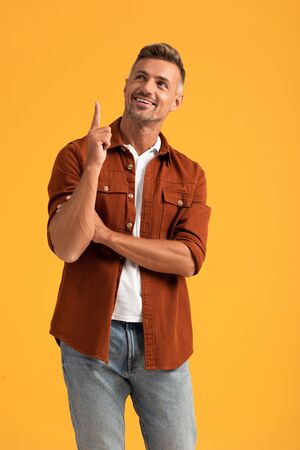 cheerful man pointing with finger and looking up isolated on orangeの写真素材