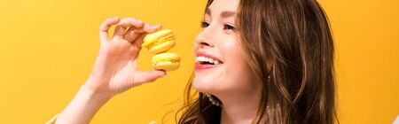 panoramic shot of happy woman holding macarons on yellow
