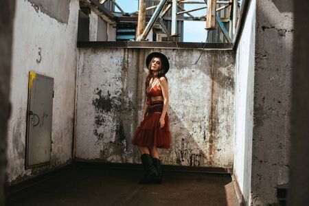 beautiful fashionable woman posing in red skirt, bra and hat on roofの写真素材