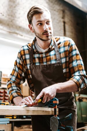 handsome carpenter holding chisel while carving wood in workshopの写真素材
