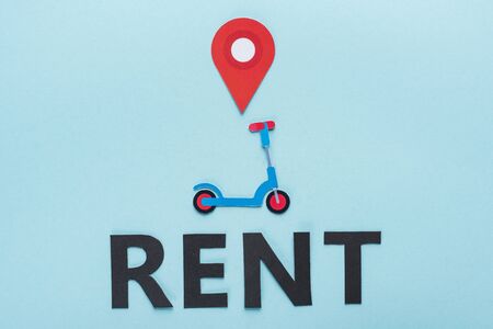 top view of paper cut kick scooter with location mark near black rent lettering on blue backgroundの写真素材