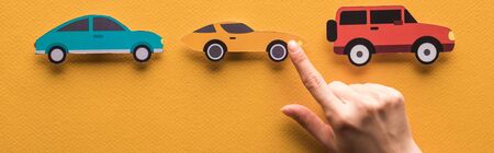 cropped view of woman pointing with finger at paper cut cars on orange background, panoramic shotの写真素材