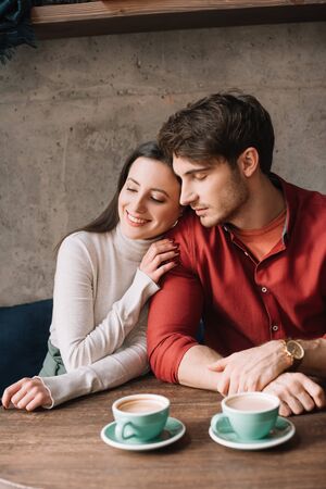 smiling tender young couple hugging and drinking coffee in coffee shopの写真素材