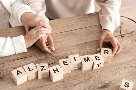 cropped view of retired couple sitting near wooden cubes with alzheimer lettersの写真素材