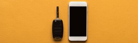 top view of car key and smartphone with blank screen on orange background with copy space, panoramic shotの写真素材