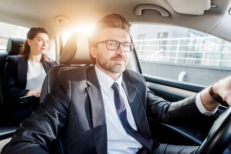 cheerful diplomat driving car and looking at camera near woman
